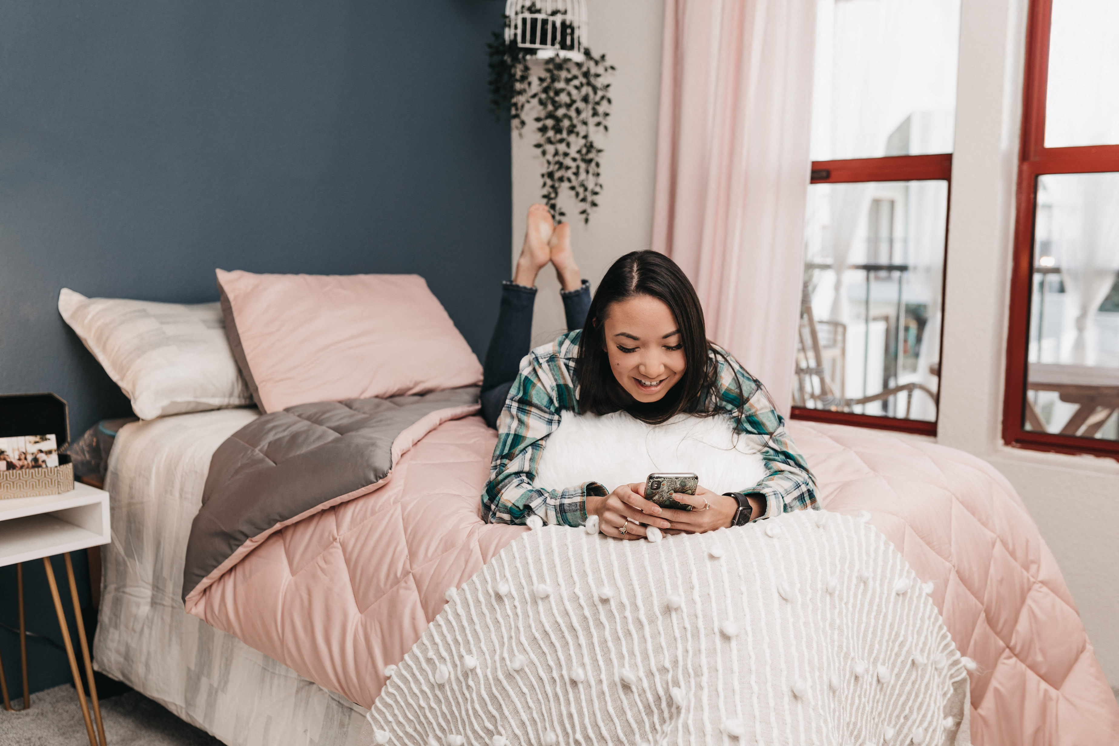 Young woman on a bed, on her phone smiling